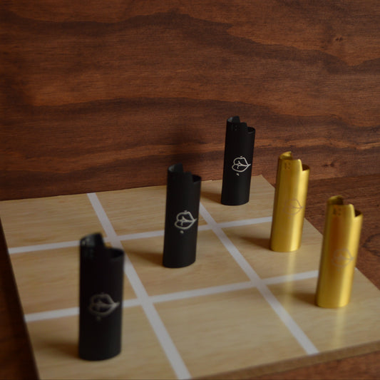 metal black and gold lighters on a light brown wood tic tac toe board with dark brown wood background